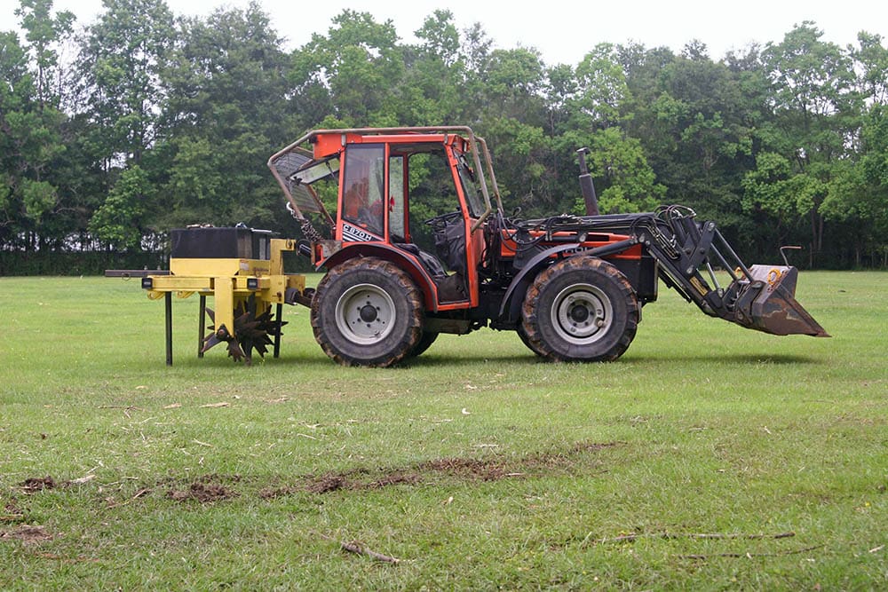 A tractor is parked in the grass near some trees.