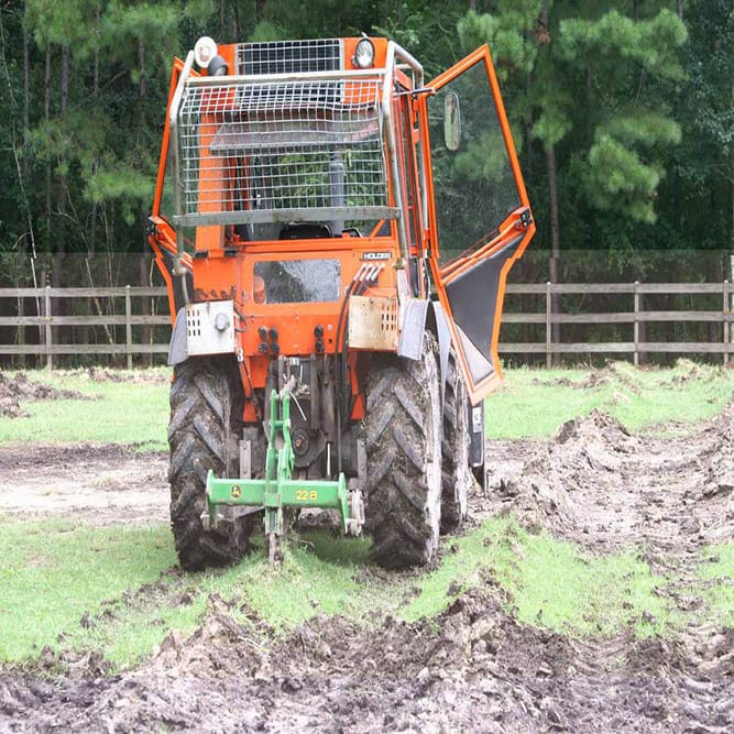 A tractor is parked in the mud near some trees.